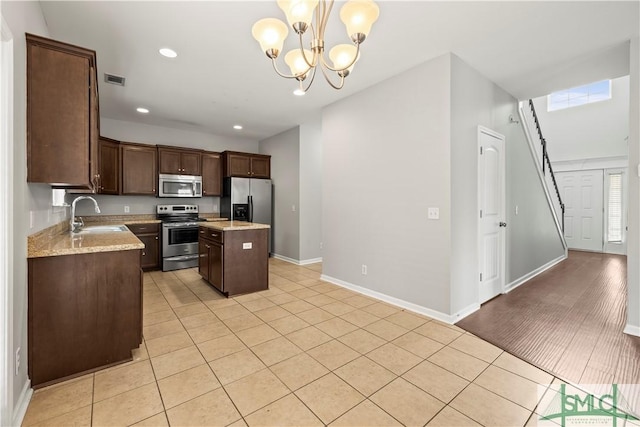 kitchen with a kitchen island, a sink, stainless steel appliances, dark brown cabinetry, and pendant lighting