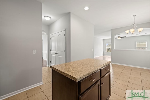 kitchen featuring a kitchen island, light tile patterned flooring, dark brown cabinets, decorative light fixtures, and ceiling fan with notable chandelier