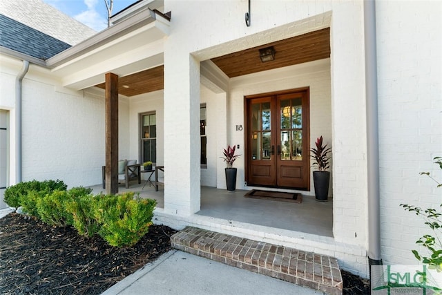 entrance to property featuring brick siding, covered porch, french doors, and roof with shingles