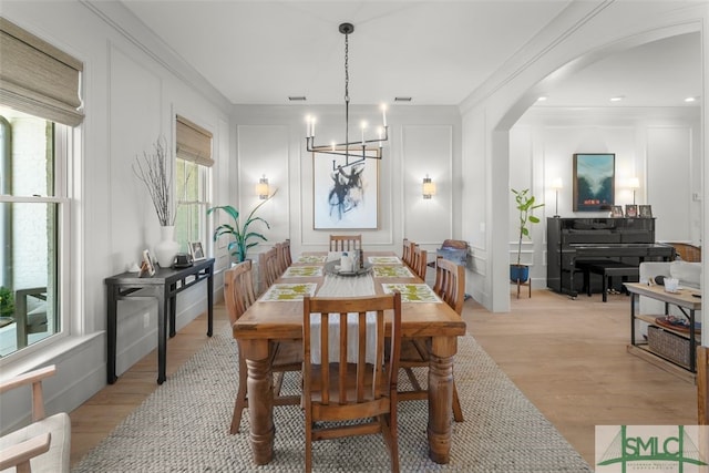 dining room featuring a decorative wall, a notable chandelier, light wood-style flooring, and arched walkways