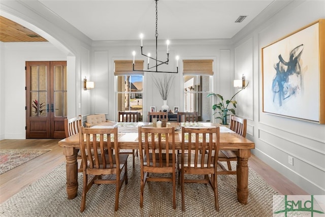 dining room featuring light wood-type flooring, visible vents, arched walkways, a decorative wall, and a chandelier