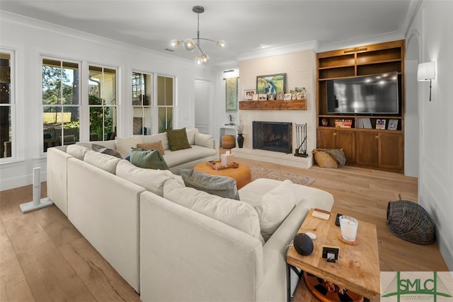 living area featuring built in shelves, light wood finished floors, an inviting chandelier, a fireplace, and crown molding