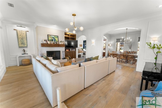 living room with an inviting chandelier, a decorative wall, arched walkways, and ornamental molding