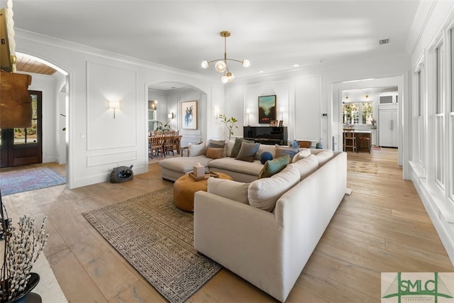 living area featuring light wood finished floors, crown molding, an inviting chandelier, arched walkways, and a decorative wall