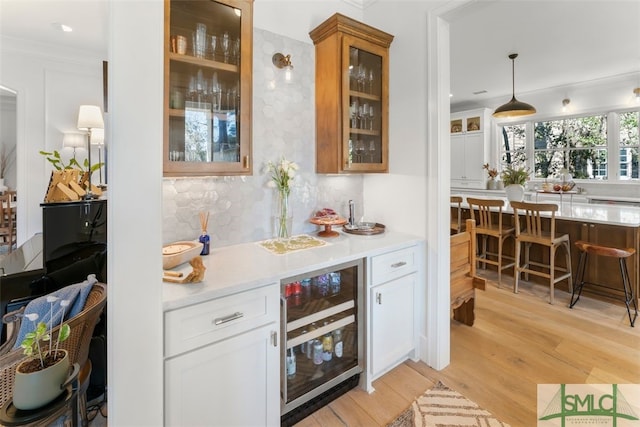 bar featuring beverage cooler, ornamental molding, a bar, light wood-style floors, and backsplash