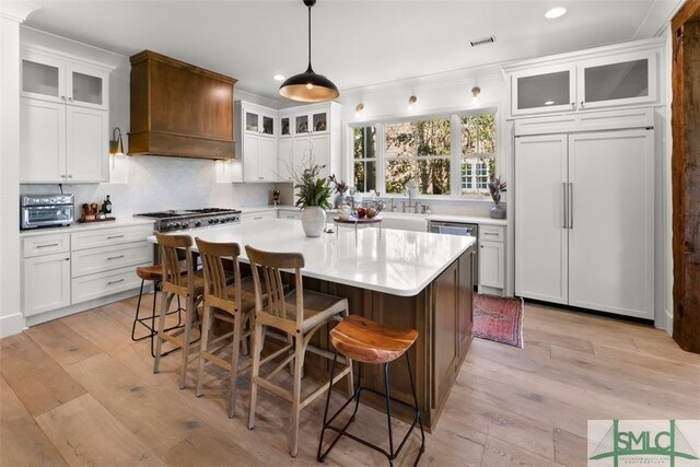 kitchen with visible vents, premium range hood, light countertops, stove, and paneled fridge