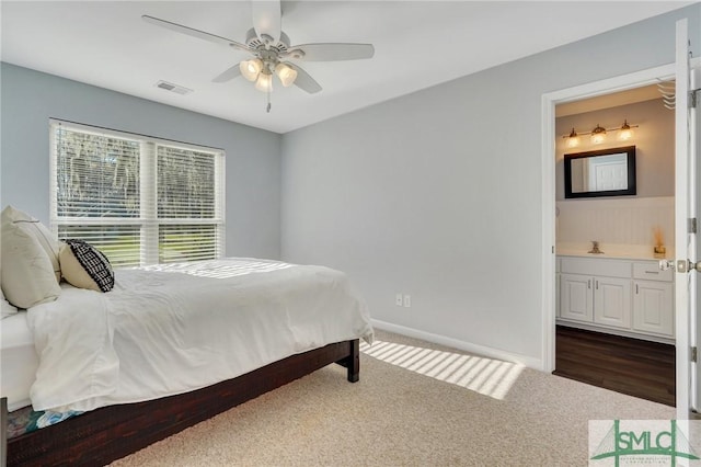 bedroom with a ceiling fan, baseboards, visible vents, ensuite bath, and dark colored carpet