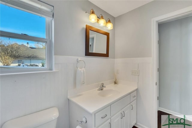 half bathroom with vanity, toilet, and wainscoting