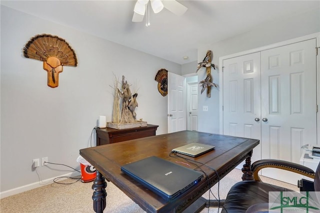 carpeted office space featuring baseboards and a ceiling fan