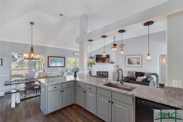 kitchen with a sink, a glass covered fireplace, lofted ceiling, dishwasher, and light stone countertops