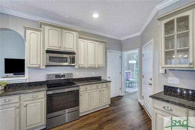 kitchen featuring dark wood-style floors, dark stone counters, ornamental molding, glass insert cabinets, and appliances with stainless steel finishes