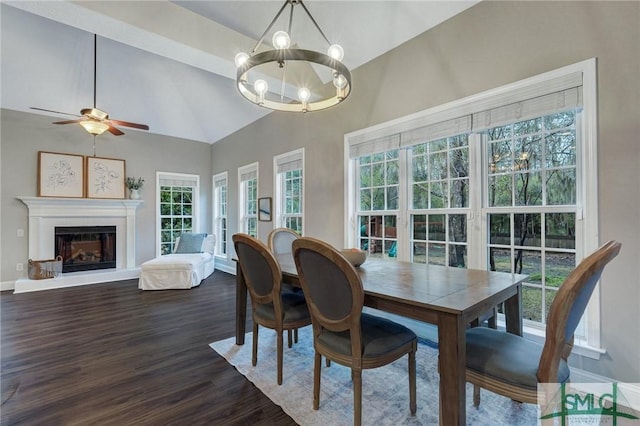 dining area featuring dark wood-style floors, baseboards, vaulted ceiling, a glass covered fireplace, and ceiling fan with notable chandelier