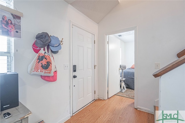 entryway with light wood-style flooring, a textured ceiling, and vaulted ceiling