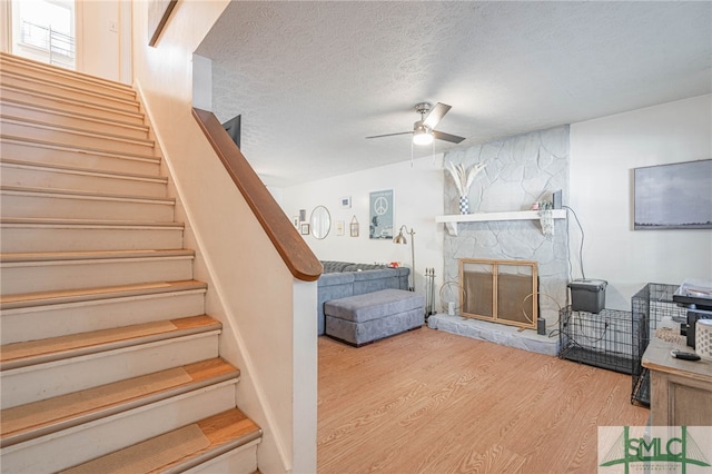 stairway with a stone fireplace, a textured ceiling, a ceiling fan, and wood finished floors