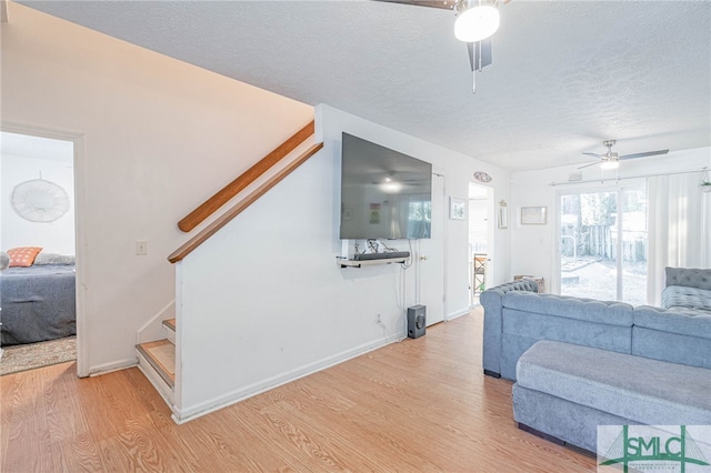 living room featuring stairway, a ceiling fan, baseboards, a textured ceiling, and light wood-type flooring