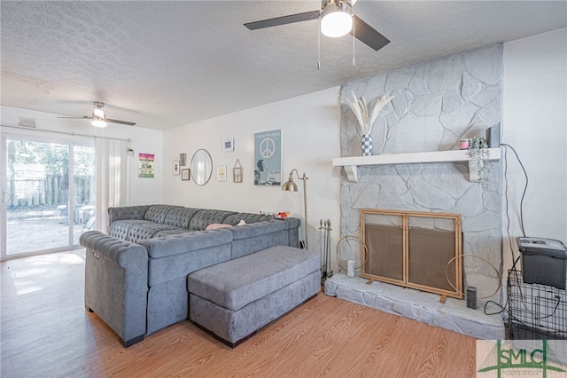 living room with ceiling fan, a textured ceiling, a stone fireplace, and wood finished floors