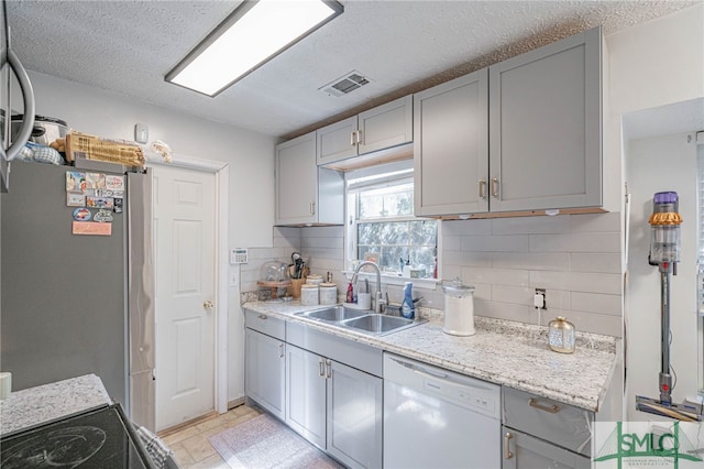 kitchen with visible vents, gray cabinetry, dishwasher, freestanding refrigerator, and a sink