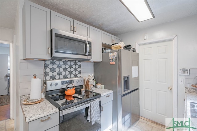 kitchen with decorative backsplash, gray cabinets, appliances with stainless steel finishes, and a textured ceiling