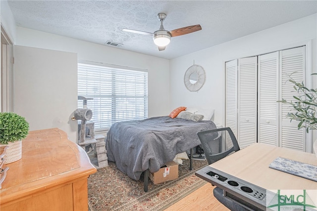 bedroom with visible vents, ceiling fan, wood finished floors, a closet, and a textured ceiling