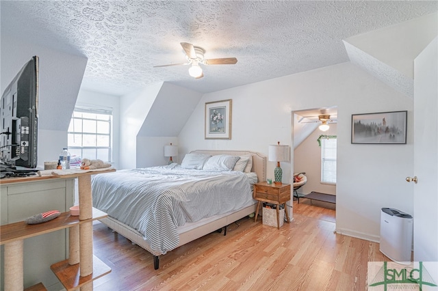 bedroom with a textured ceiling, vaulted ceiling, light wood-style flooring, and ceiling fan