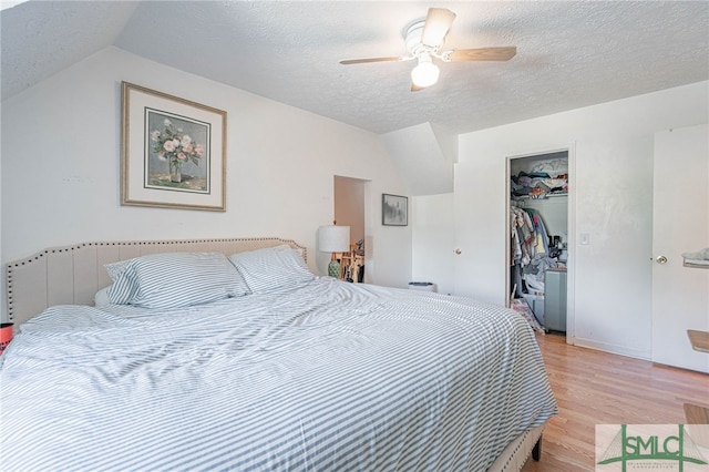 bedroom with a ceiling fan, vaulted ceiling, a closet, a textured ceiling, and light wood-type flooring