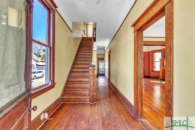 hall featuring baseboards, a healthy amount of sunlight, stairs, and hardwood / wood-style flooring