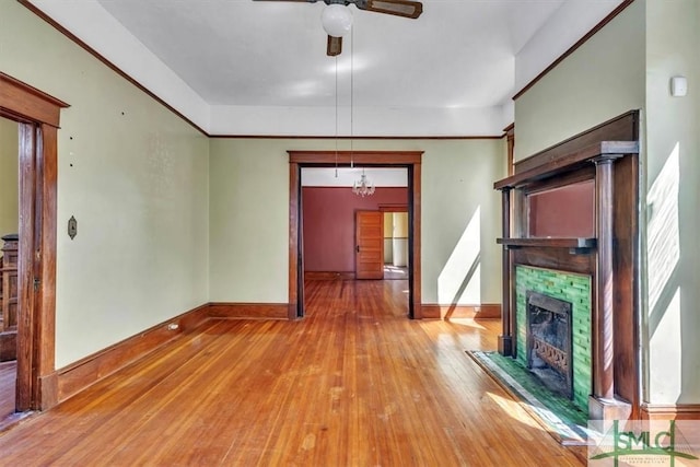 unfurnished living room featuring baseboards, light wood-style flooring, a tiled fireplace, and ceiling fan with notable chandelier