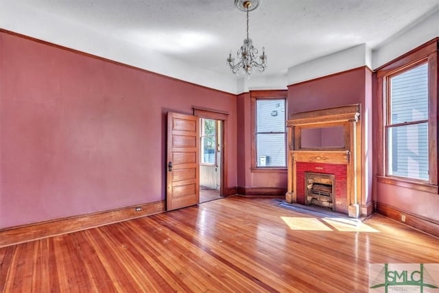 unfurnished living room with an inviting chandelier, a fireplace, baseboards, and wood-type flooring