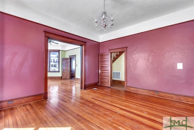 spare room with visible vents, baseboards, light wood finished floors, a textured ceiling, and a chandelier