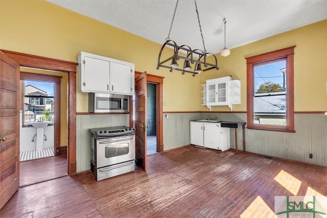 kitchen with wainscoting, stainless steel appliances, white cabinetry, wood-type flooring, and a sink