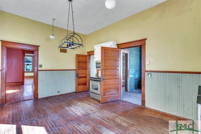 unfurnished room with a wainscoted wall, lofted ceiling, and dark wood finished floors