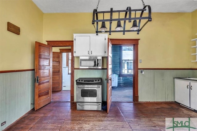 kitchen with a wainscoted wall, appliances with stainless steel finishes, white cabinets, and dark wood-style flooring