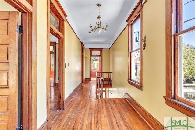 corridor with an upstairs landing, a notable chandelier, plenty of natural light, and hardwood / wood-style flooring