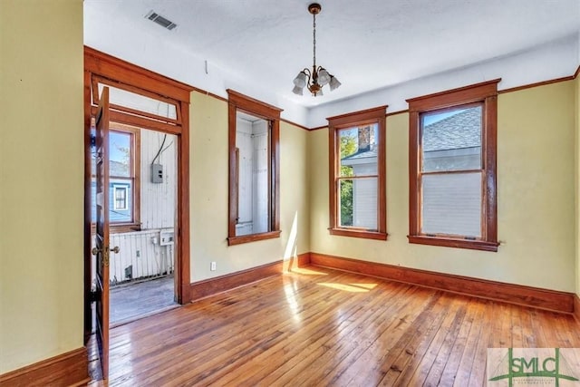 spare room featuring a chandelier, visible vents, baseboards, and hardwood / wood-style flooring