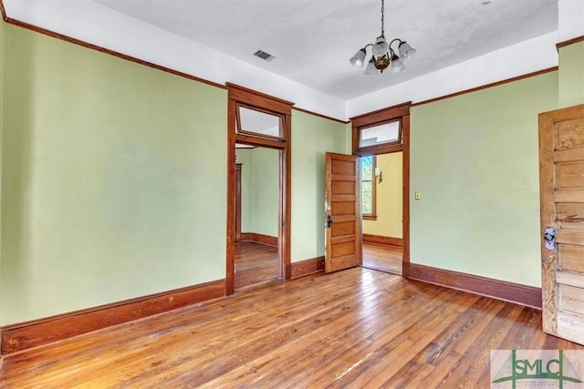 empty room featuring visible vents, wood-type flooring, a notable chandelier, and baseboards