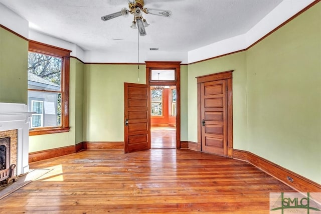 unfurnished living room featuring hardwood / wood-style floors, a ceiling fan, visible vents, baseboards, and a fireplace with flush hearth