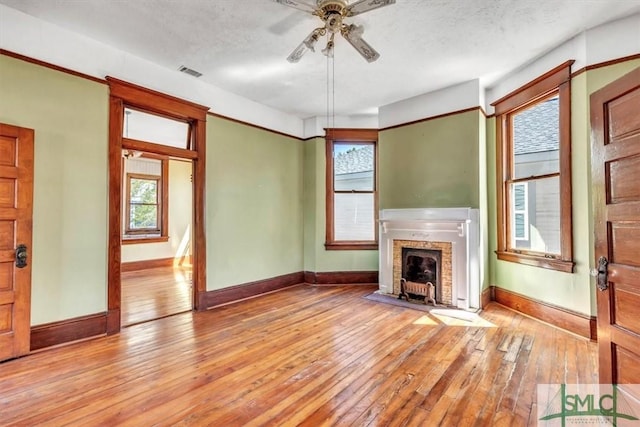 unfurnished living room with light wood finished floors, visible vents, a healthy amount of sunlight, and a fireplace