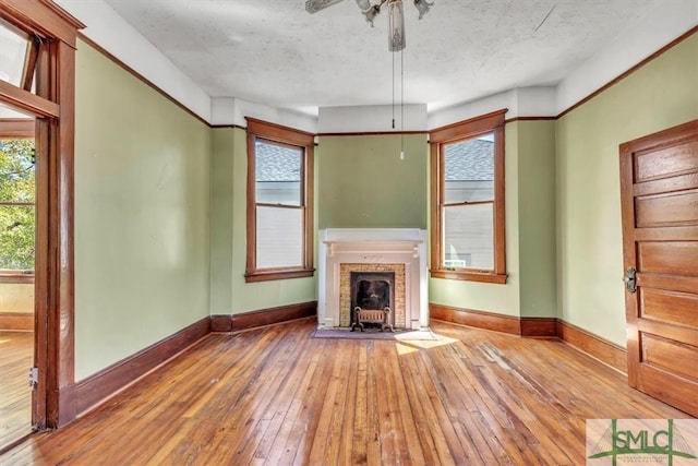 unfurnished living room featuring hardwood / wood-style flooring, a ceiling fan, baseboards, and a textured ceiling