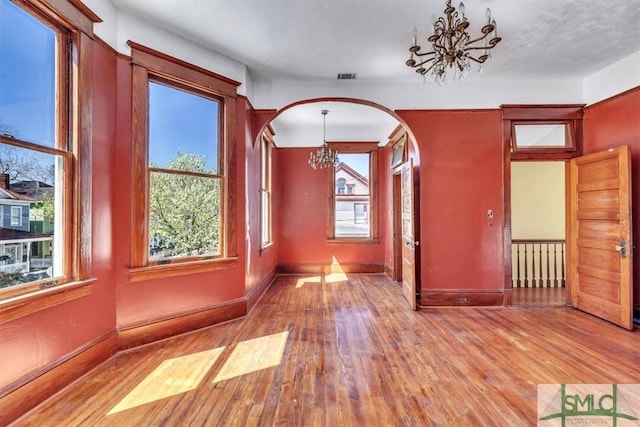 unfurnished dining area featuring visible vents, baseboards, wood finished floors, arched walkways, and a notable chandelier