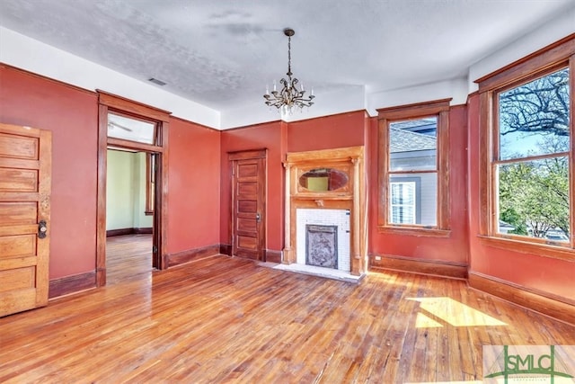 unfurnished living room featuring a fireplace, baseboards, light wood finished floors, and a chandelier