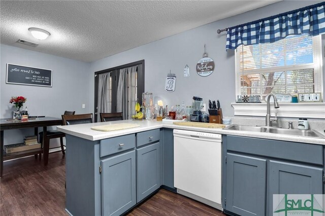 kitchen featuring visible vents, dark wood finished floors, dishwasher, a peninsula, and a sink