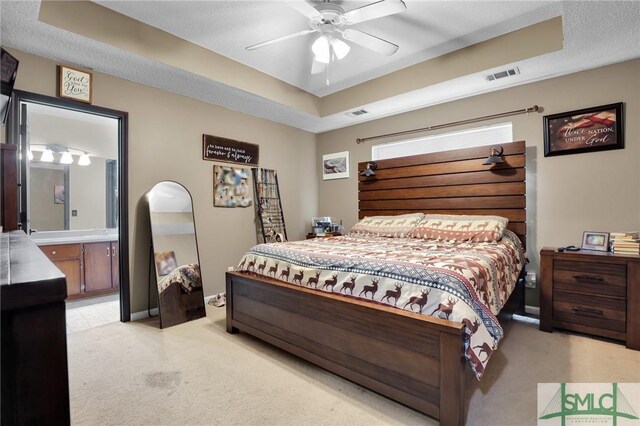 bedroom with visible vents, a raised ceiling, light colored carpet, and ensuite bathroom