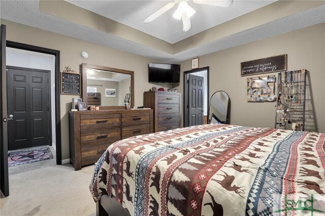 bedroom with a ceiling fan, baseboards, a textured ceiling, a raised ceiling, and light colored carpet