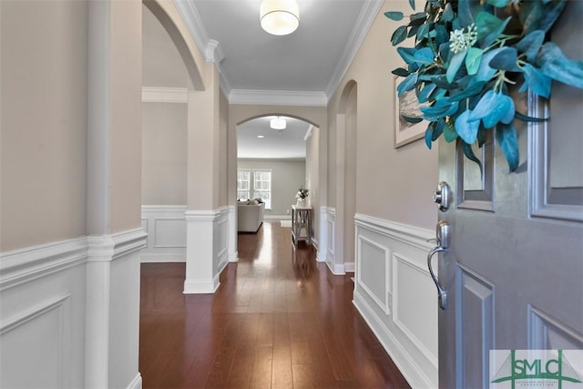 foyer entrance with a wainscoted wall, ornate columns, arched walkways, ornamental molding, and dark wood-type flooring