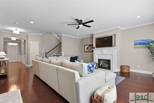 living area featuring stairway, baseboards, arched walkways, dark wood-style flooring, and crown molding