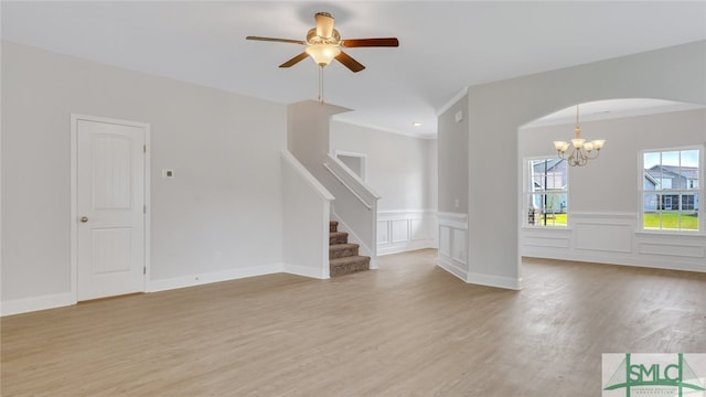 unfurnished living room featuring stairway, arched walkways, ceiling fan with notable chandelier, and light wood finished floors