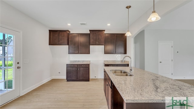 kitchen featuring visible vents, light wood-type flooring, a sink, dark brown cabinetry, and decorative backsplash