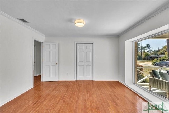 empty room with visible vents, baseboards, light wood-style floors, and ornamental molding