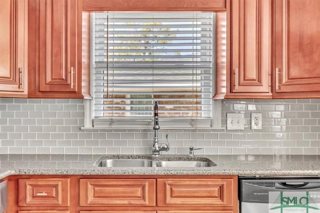 kitchen with dishwashing machine, light stone countertops, tasteful backsplash, and a sink