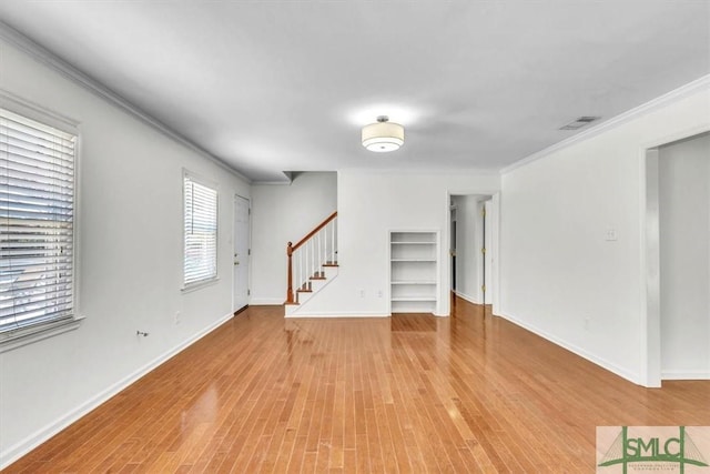 unfurnished living room featuring built in features, wood finished floors, stairway, crown molding, and baseboards